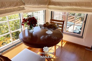 Un coin repas avec une table ronde, un vase rempli de fleurs rouges et un panier de pain.