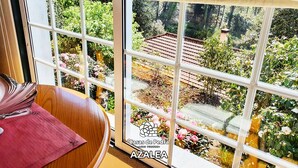 A room with a large window overlooking a garden with flowers and a tiled roof structure.