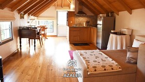 A spacious loft-style room with a high ceiling, wooden beams, a dining area, kitchen, and a cozy seating area.