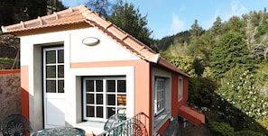 A small, single-story building with a red and white facade, a tiled roof, and a patio area with two metal chairs and a table.