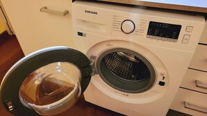 Samsungin pesukone, jossa on läpinäkyvä luukku, ohjauspaneeli ja pieni vesisäiliö.