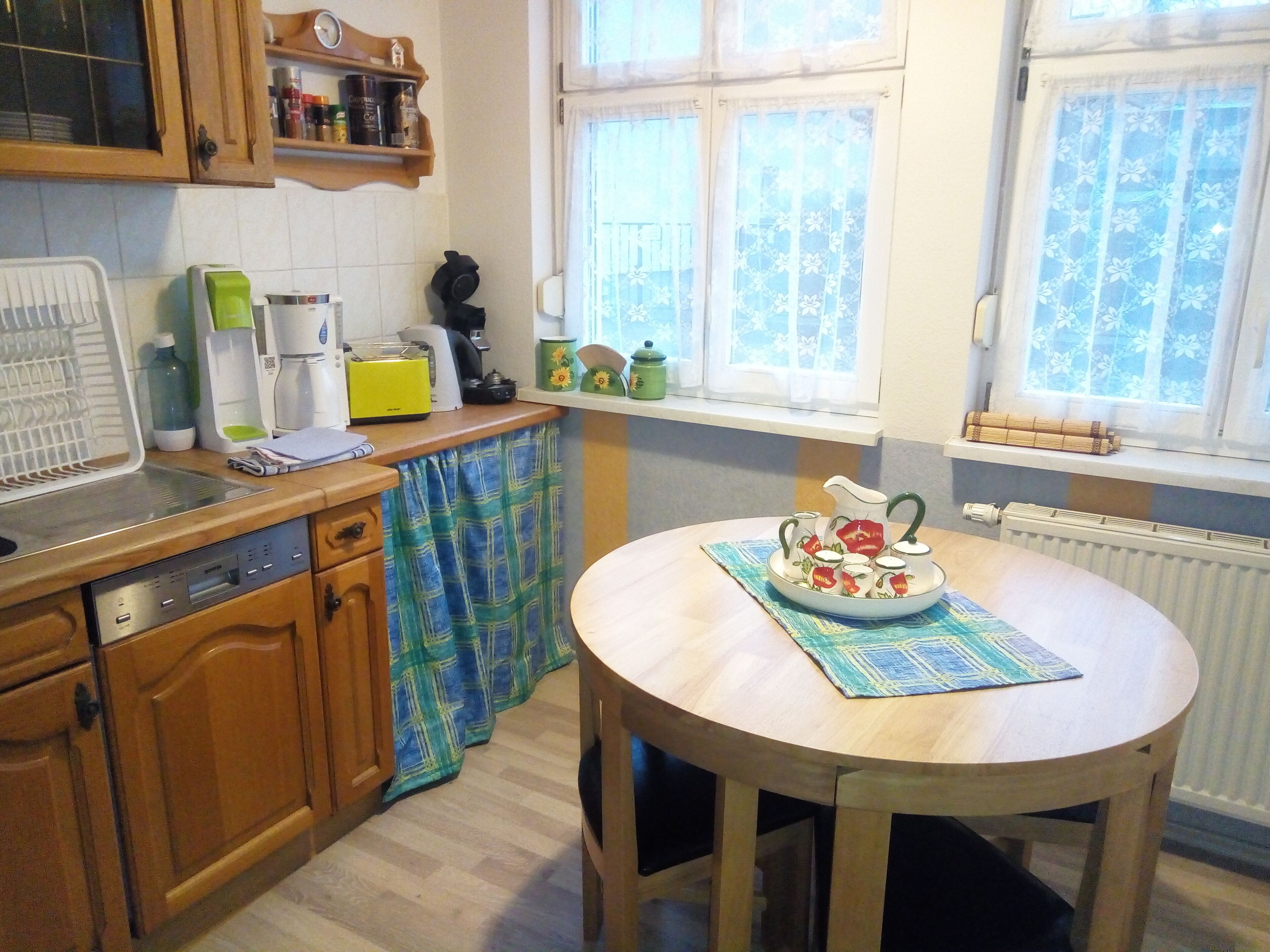 A kitchen with wooden cabinets, a coffee maker, a toaster, and a table with a floral tablecloth.
