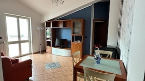 Un'ampia zona giorno con tavolo e sedie, un divano rosso, televisione e ventilatore a soffitto.