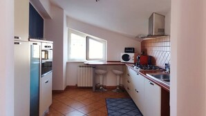 Una cucina compatta con frigorifero, fornello, microonde e una finestra che lascia entrare luce naturale.