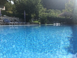 Une piscine d’un bleu éclatant, dotée de chaises longues et bordée d’un mur en pierre.