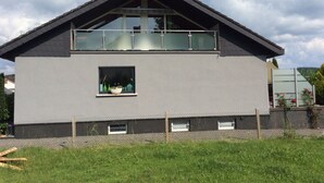 A modern two-story house with a balcony, a window with a plant, and a clear sky. - Modern and spacious attic apartment in Abtsteinach im Odenwald (Abtsteinach)