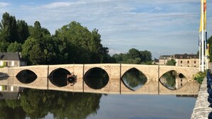 A stone bridge with multiple arches over a calm body of water, surrounded by trees and buildings. - The Périgord houses on the abbey side  (Terrasson-Lavilledieu)