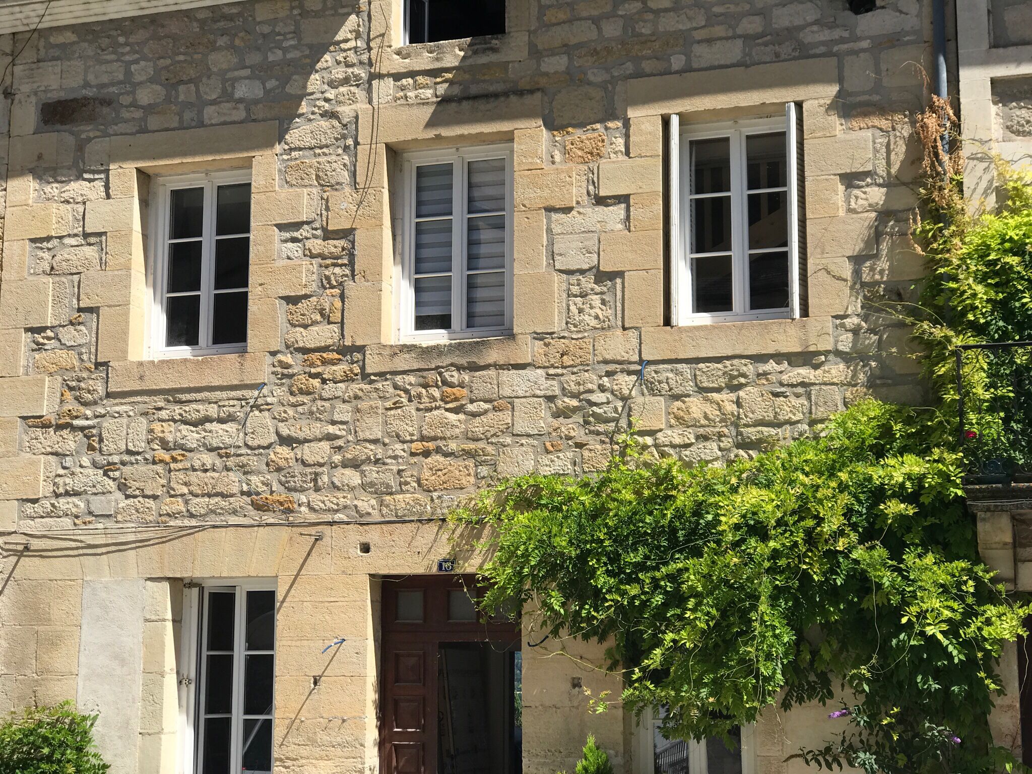 Un bâtiment en pierre avec trois fenêtres et une porte, entouré de verdure.