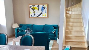 A living room with a teal sofa, a coffee table, and a painting on the wall. A staircase is visible to the right. - The Périgord houses on the abbey side  (Terrasson-Lavilledieu)