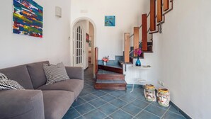A living room with a gray sofa, a colorful abstract painting, and a staircase with wooden railings. - Blue 54 - Seaside house with terraces overlooking the sea, Etna and Taormina (Pozzillo)