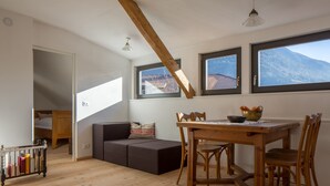 Uma sala de jantar com mesa e cadeiras de madeira, um sofá e vista para montanhas através de grandes janelas.