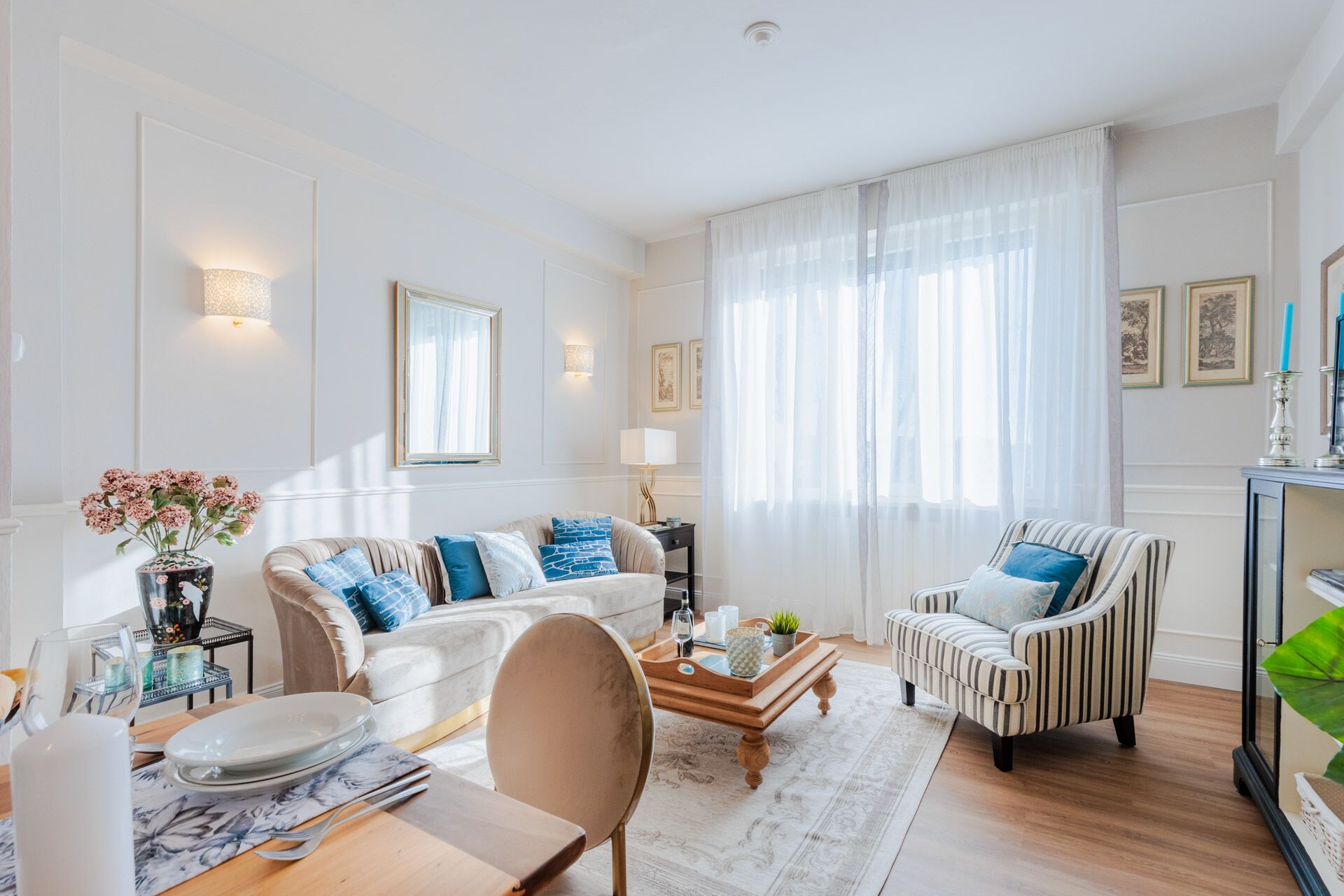 Ein helles Wohnzimmer mit Sofa, Sessel, Couchtisch und Essbereich.