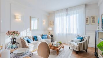Ein helles Wohnzimmer mit Sofa, Sessel, Couchtisch und Essbereich.
