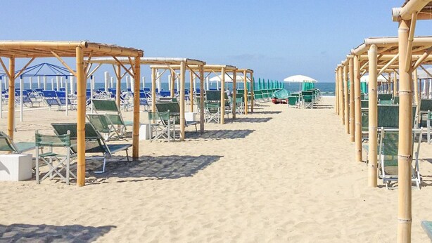 Ein Strand mit Reihen von Liegestühlen und Sonnenschirmen, einem klaren Himmel und einem Sandweg, der zum Meer führt.