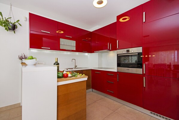 Une cuisine avec des meubles de couleur rouge, un plan de travail blanc et un four de marque Bosch.