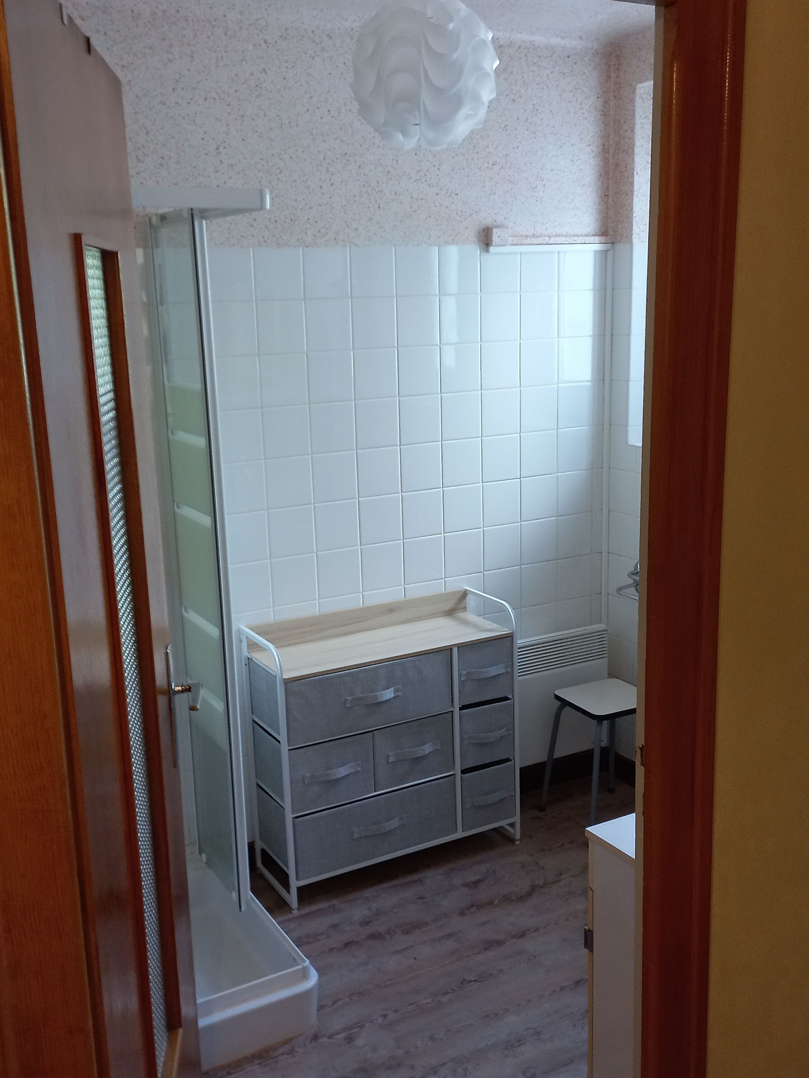 Ein Badezimmer mit weißen Fliesen, einem Holzkosmetikschrank und einem kleinen Hocker.