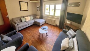 Ein Wohnzimmer mit grauem Sofa, einem Couchtisch, einem Fernseher und einem Fenster mit Vorhängen.