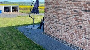 A brick building with a covered patio area, a garage, and a view of a green field. - modern and cozy apartment on the Edersee (Waldeck)