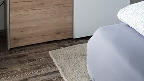 A room with a wooden wardrobe, a white cabinet, and a patterned bed. - modern and cozy apartment on the Edersee (Waldeck)
