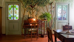 A room with a wooden table, chairs, and a lamp. There is a wall with a tree mural and a door with a stained glass window. - Picturesque apartment in a medieval village perched at top a mountain ridge (Imperia)