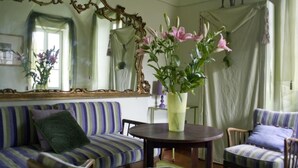 A room with a striped sofa, a round table, and chairs. There is a mirror with an ornate frame and a vase with flowers on the table. - Picturesque apartment in a medieval village perched at top a mountain ridge (Imperia)