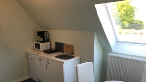 A compact kitchen with a white countertop, a microwave, and a coffee maker. There's a window with a view of trees and a radiator.