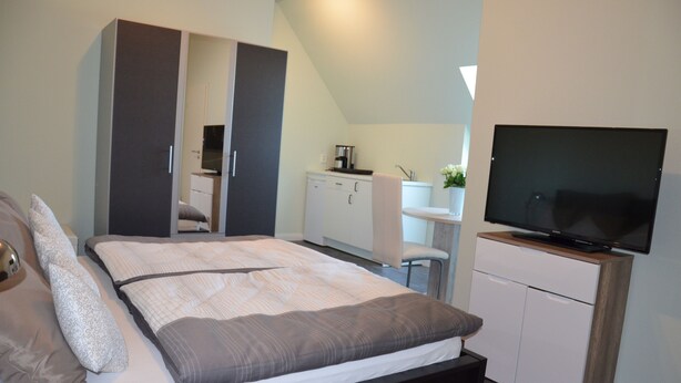 A bedroom with a bed, a wardrobe, a television, and a kitchenette.