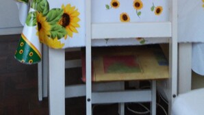 Um quarto pequeno com uma mesa e cadeira brancas, um armário branco e uma parede amarela.