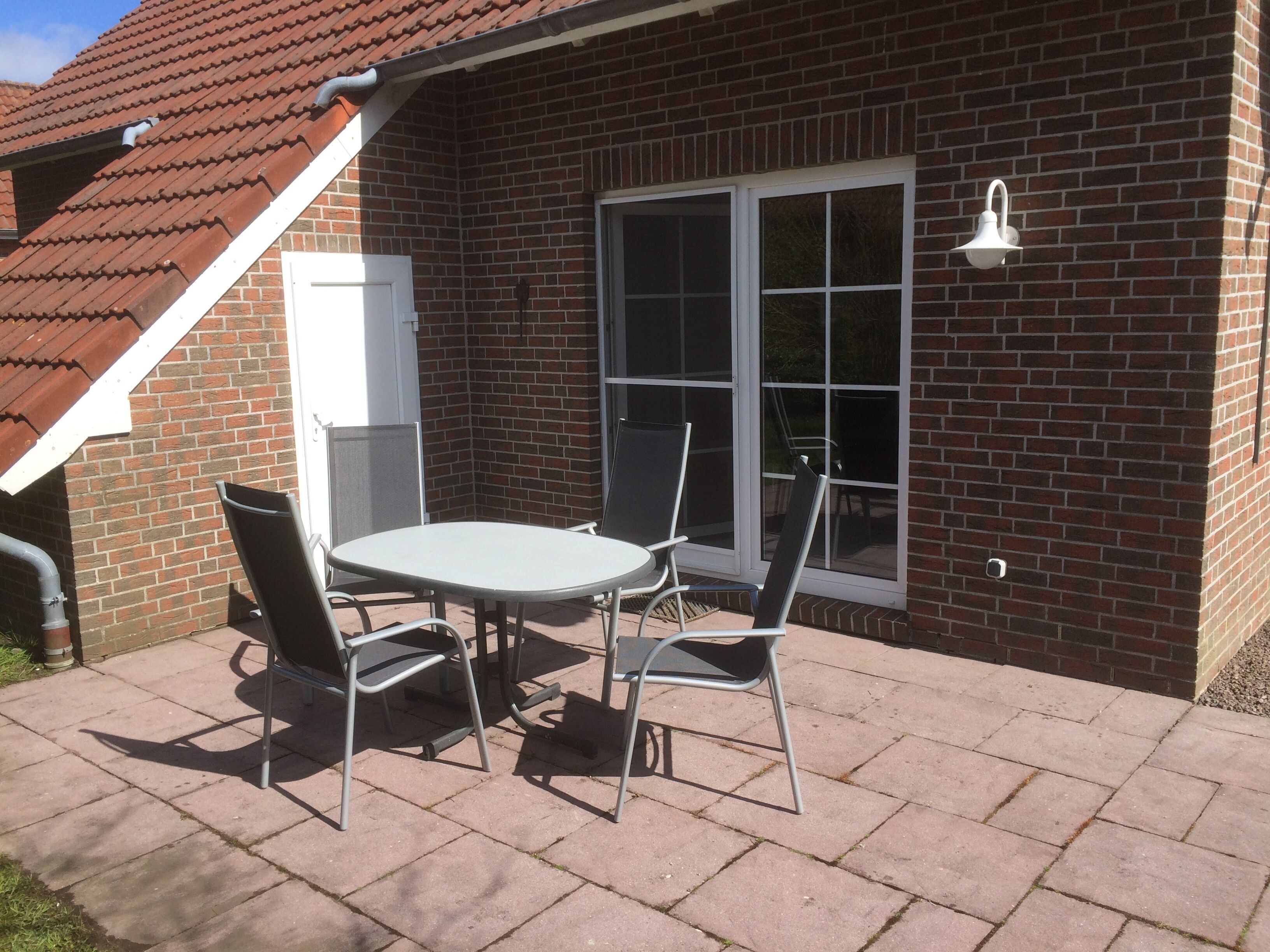 A patio with a table and chairs, a brick wall, and a window.