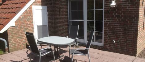 A patio with a table and chairs, a brick wall, and a window.