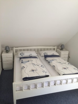 Un lit simple décoré sur le thème de la marine, deux tables de chevet avec des lampes et un mur blanc uni.