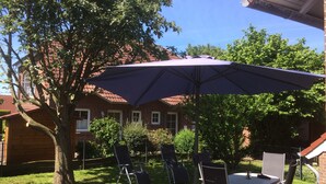 Un espace patio avec une table et des chaises, un grand parasol et un arbre.