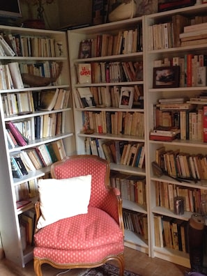 Une pièce comprenant un fauteuil à revêtement rouge, une bibliothèque remplie de livres et une petite table avec une lampe.