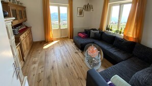 A living room with a dark sofa, a glass coffee table, wooden cabinets, and a view of the outdoors through a sliding door.