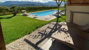 A covered outdoor area with a pool, lounge chairs, and a view of mountains.