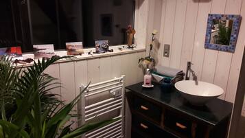 A bathroom with a white sink, a mirror with a mosaic frame, and a towel rack. There is a potted plant in the corner and a window with a view of the outside.