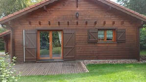 A wooden cabin with a sloped roof, a sliding glass door, and a window with shutters.
