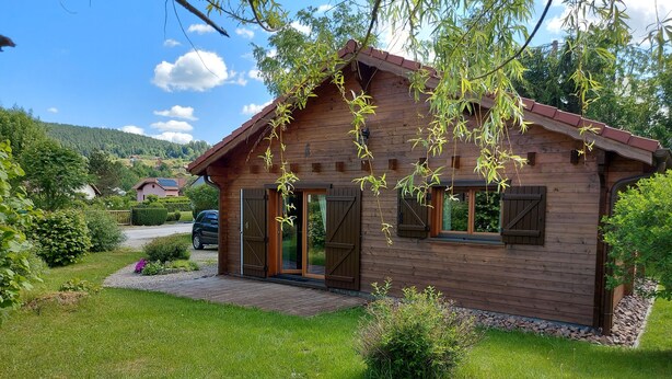 A wooden cabin with a red roof, a paved driveway, and a small garden area.