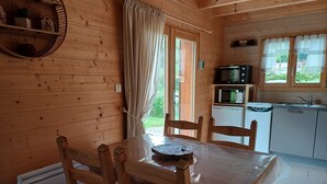 A wooden cabin with a dining table, chairs, a microwave, and a sink in the kitchen area.