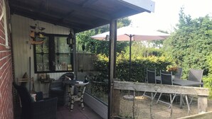 A covered patio area with wicker furniture, a grill, and a view of the garden. - "Idyllic house on the Wadden Sea - peace, nature & adventure for 2- and 4-legged friends" (Jemgum)