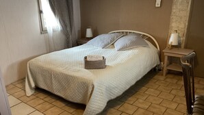 A neatly made bed with a quilted cover, a bedside table with a lamp, and a chair.