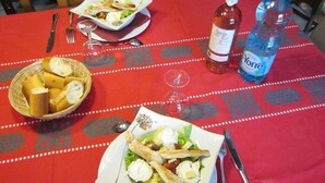 A dining table with a red tablecloth, a bottle of wine, a bottle of water, and a basket of bread.