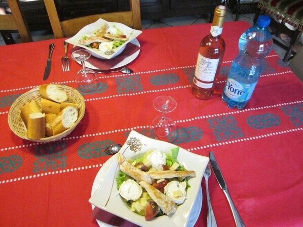 Una mesa de comedor con mantel rojo, una botella de vino, una botella de agua y una cesta de pan.