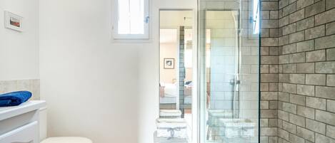 A bathroom with a white toilet, a glass shower enclosure, and a small stool with baskets.
