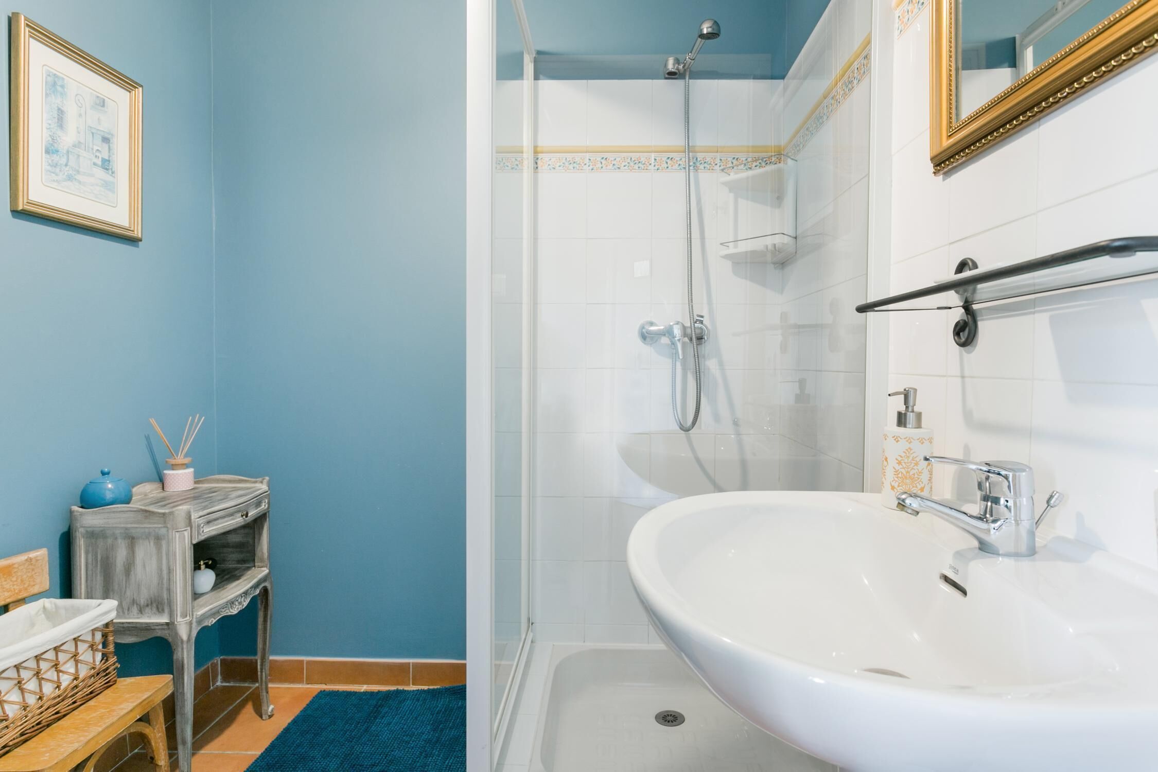 Ein Badezimmer mit weißem Waschbecken, Dusche und einem kleinen Tisch mit einer blauen Vase.
