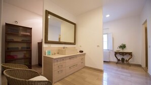 Un bagno con un grande specchio, un lavandino, sedie in vimini e un armadietto in legno.