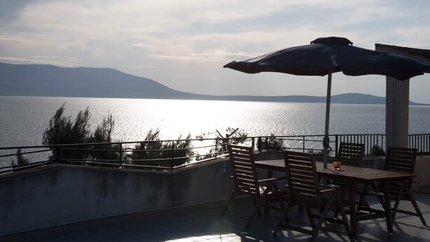 Patio esterno con tavolo e sedie, vista su un lago e montagne.