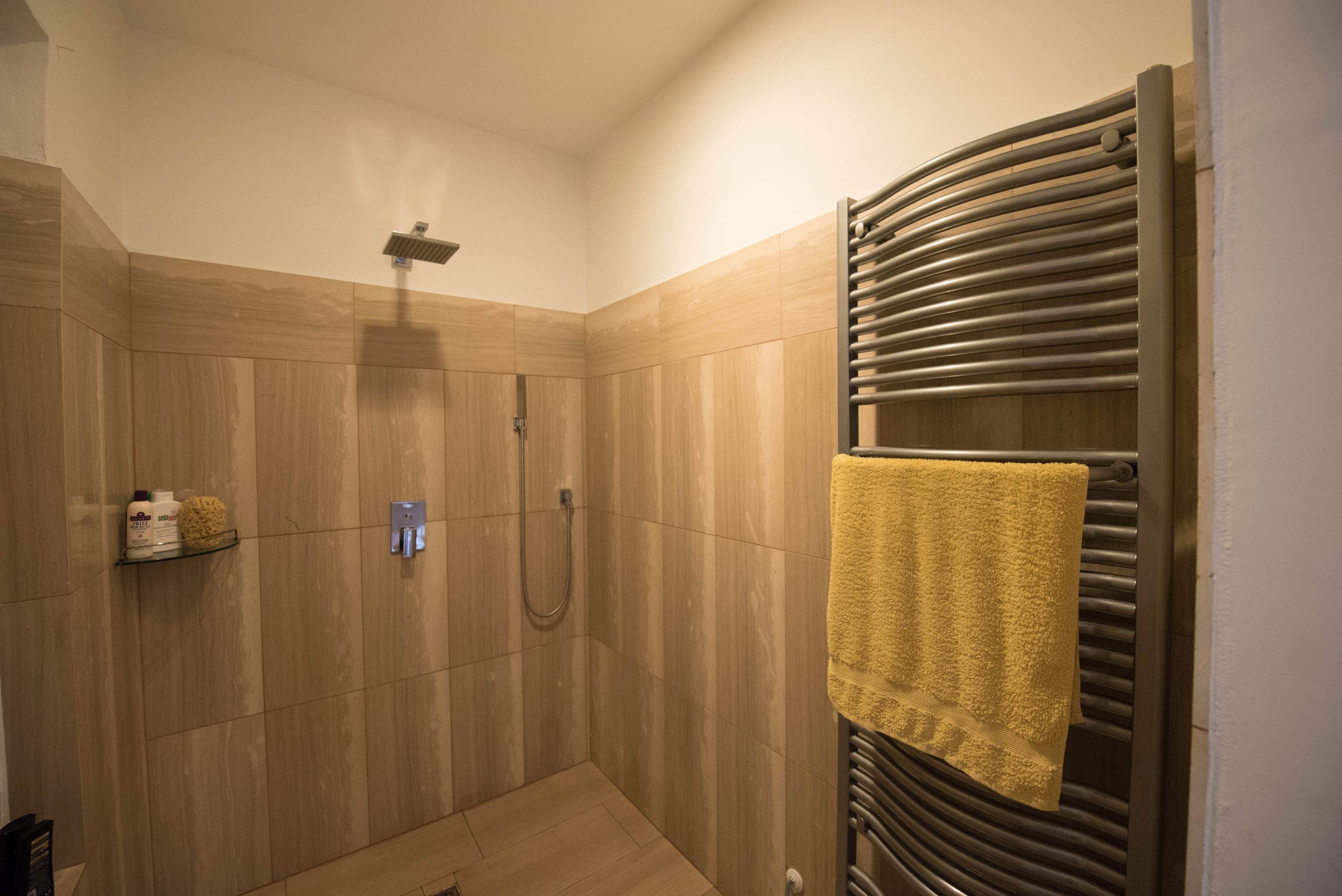 A shower area with a towel rack and a shelf with toiletries.