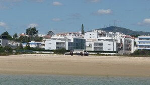 Et kysthotel med flere etager, en sandstrand i forgrunden og et bakket landskab i baggrunden.