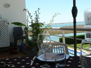 Une table à manger avec vue sur la mer, une plante en pot et un verre d’eau.